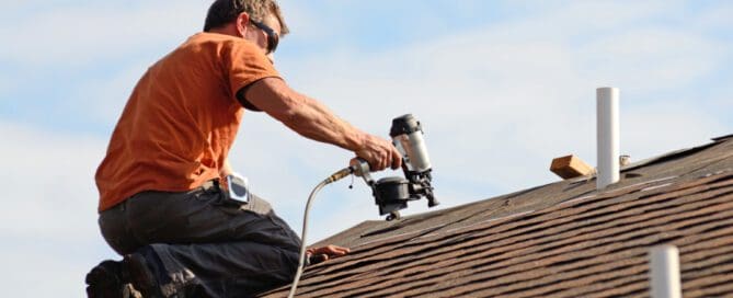 Worker using a nail gun to install shingles on a residential roof.