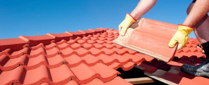 Person wearing gloves installing large red shingles on a roof