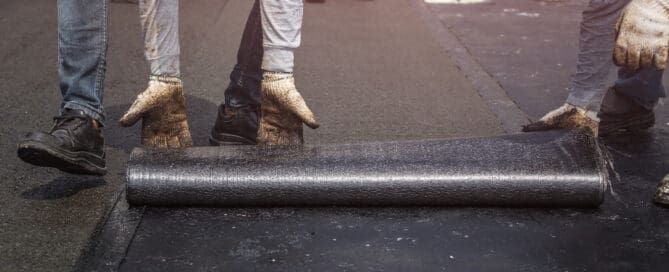 Worker installing tar foil on the rooftop of building. Waterproof system by gas and fire torching.