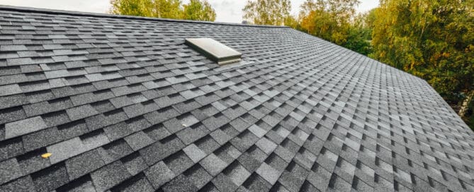 A new roof on a house with dark grey shingles, and a small skylight on the roof.