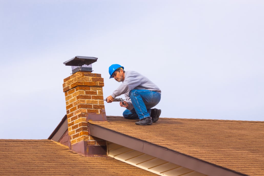 Man with blue helmet is fixing brick chimney of house