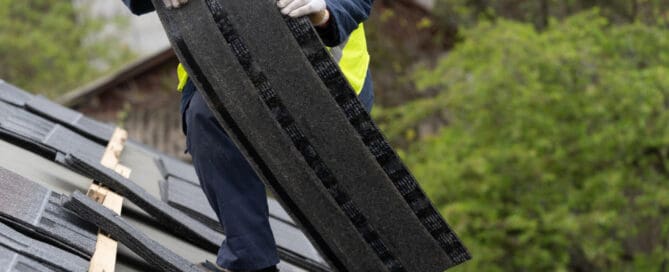 Person carrying roof panel while standing on roof and wearing reflective vest and gloves