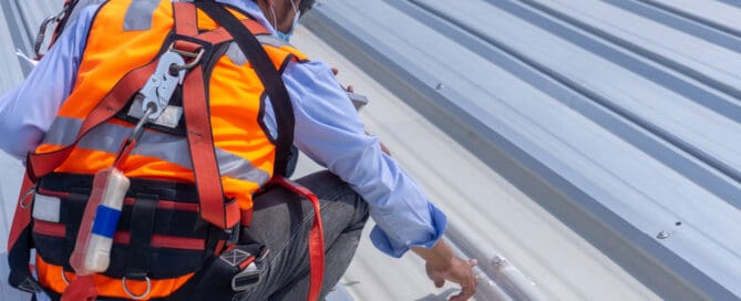 Two workers wearing safety equipment are inspecting metal roof sheet.