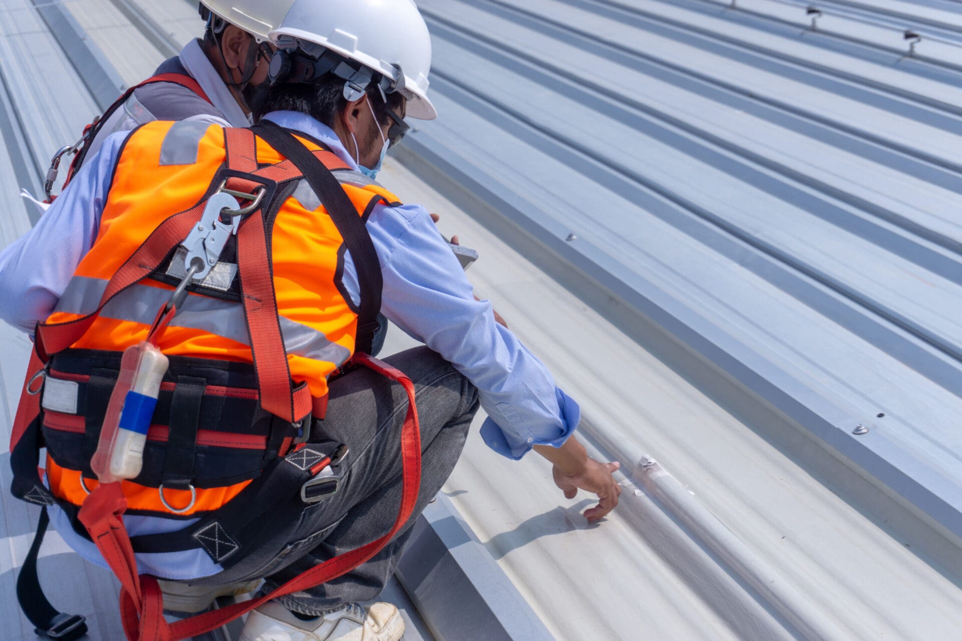 Two workers wearing safety equipment are inspecting metal roof sheet.
