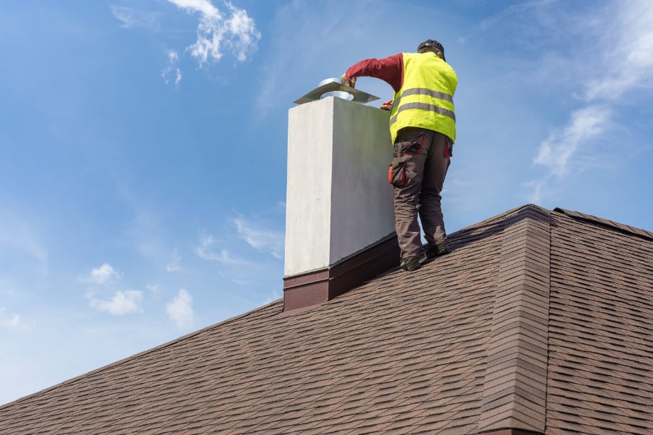 Man with yellow vest is repairing chimney in brown roof