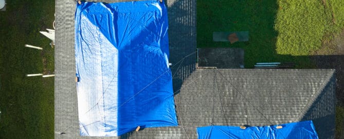 Top view of leaking house roof covered with protective tarp sheets against rain water.