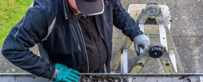Man cleaning gutters while standing on latter and wearing gloves