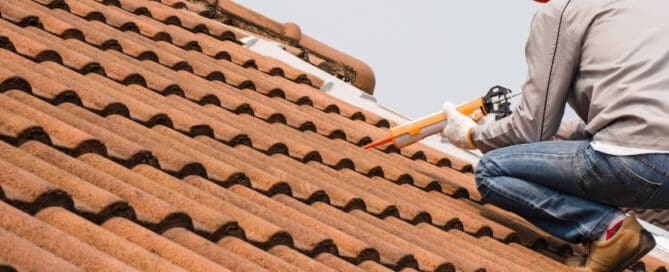 Man shingle roof, while wearing helmet.