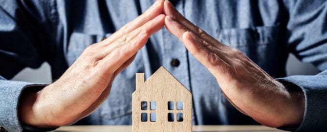 Man forming roof shape with hands over wooden toy of house, on table.