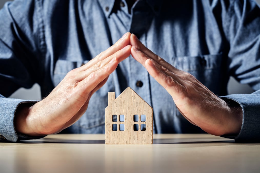 Man forming roof shape with hands over wooden toy of house, on table.