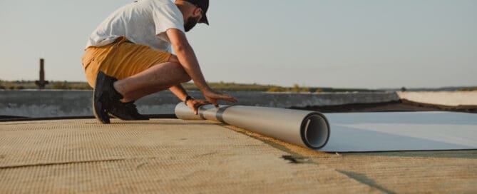 Man kneeling on as he installs TPO material on flat roof.