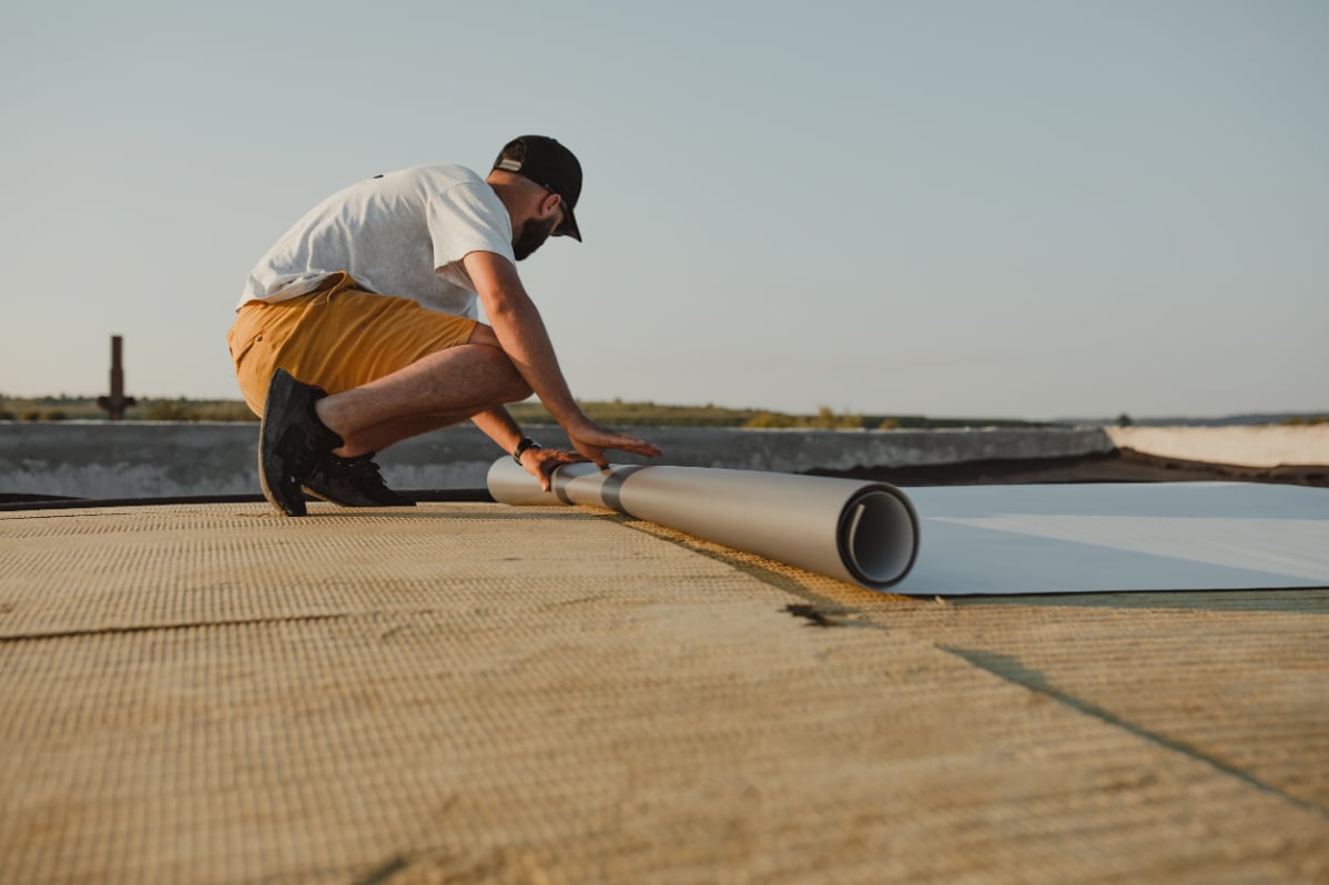Man kneeling on as he installs TPO material on flat roof.