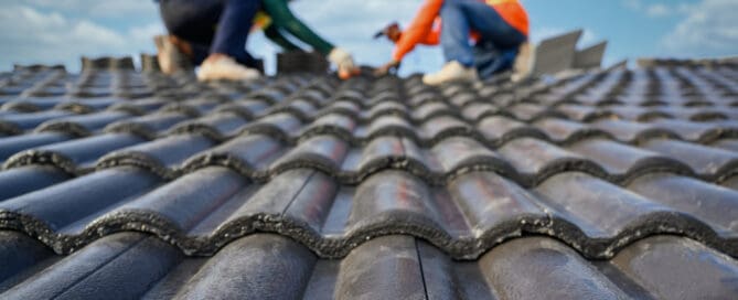 View of black roof and two blurred roofers on the background.