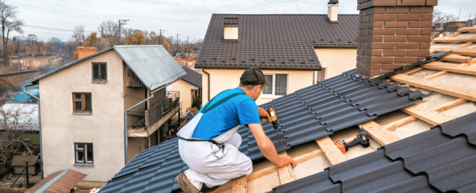 A construction worker installing metal roofing sheets on a residential home under a clear blue sky.