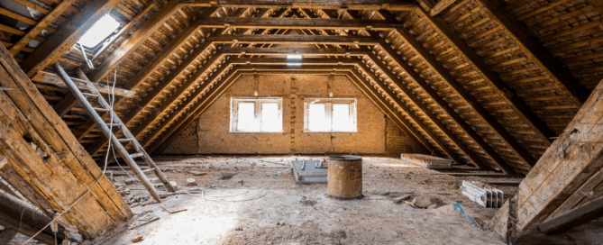 An empty attic with exposed wooden beams, brick walls, and two large rectangular windows allowing sunlight to enter. The floor is scattered with dust and debris, and a ladder leans against one of the beams.