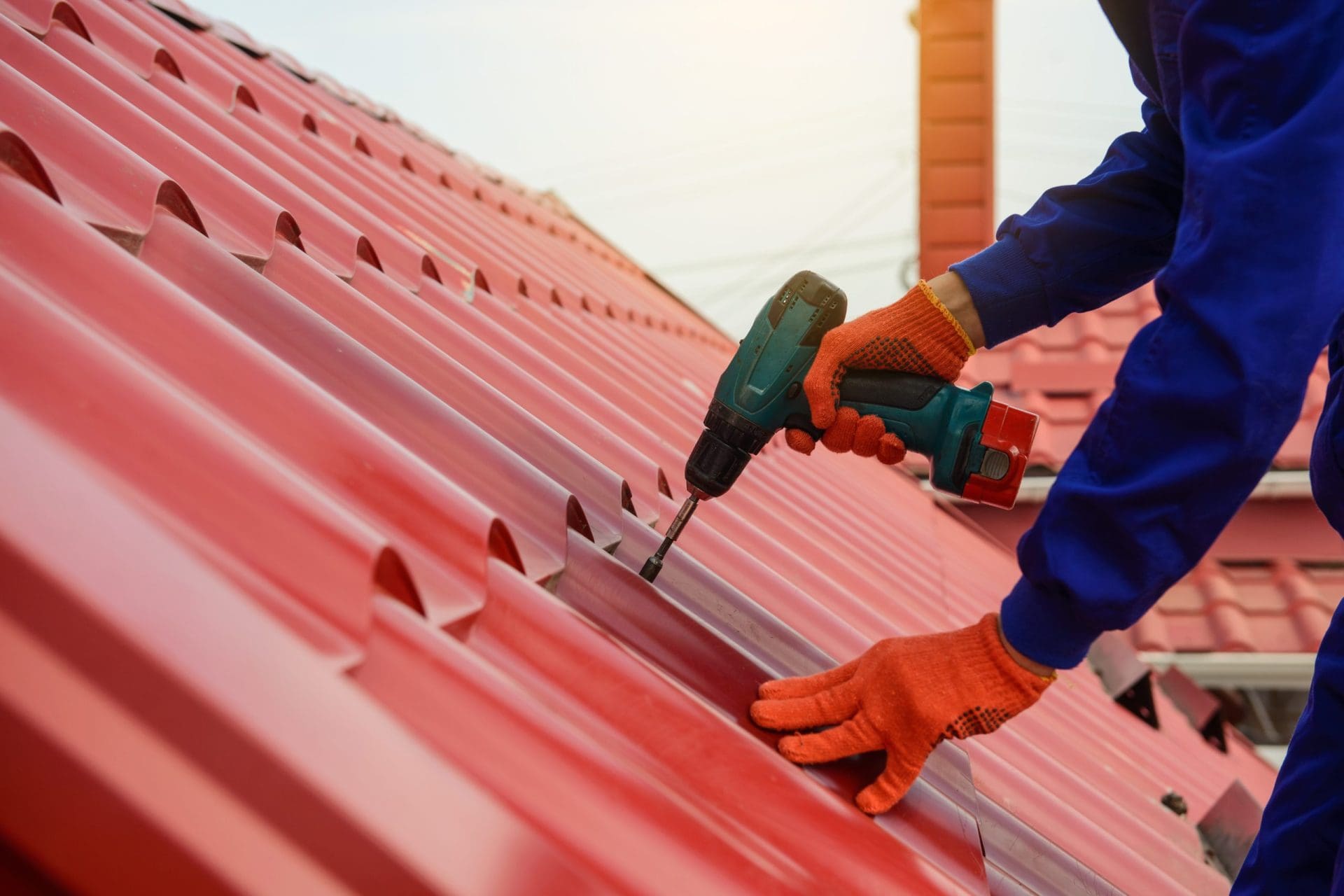 A worker is installing roofing material. They are using a power tool to screw tiles or panels in place, highlighting the process of putting in new roofing materials for a building.