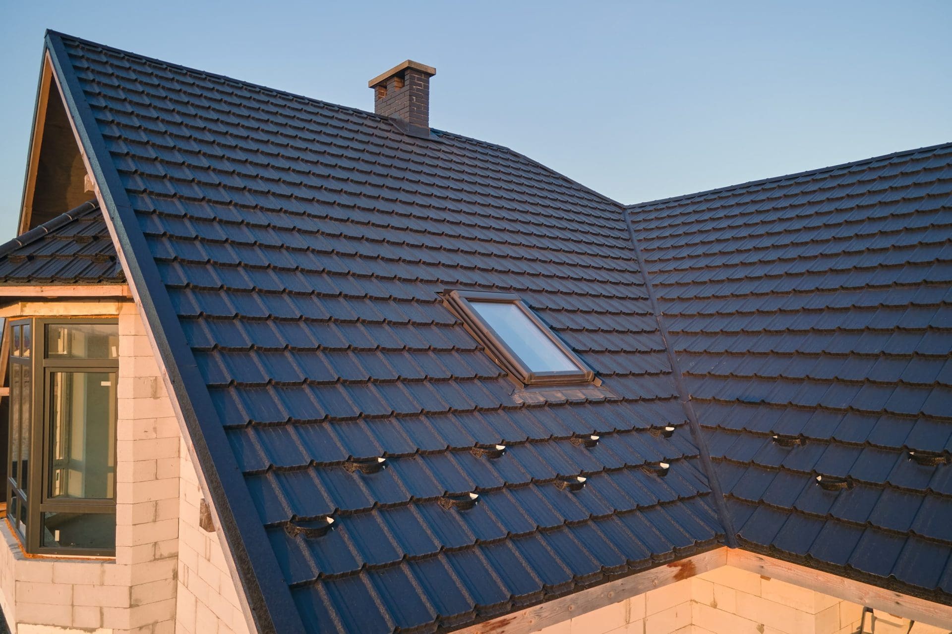 Closeup of attic window on house roof top covered with ceramic shingles. Tiled covering of building.