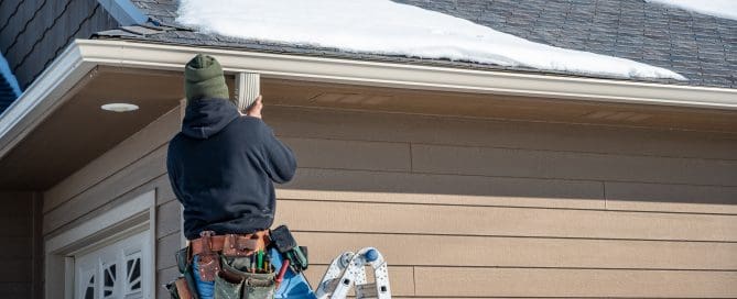 Contractor installing gutters on a residential building in the winter with snow on the roof.