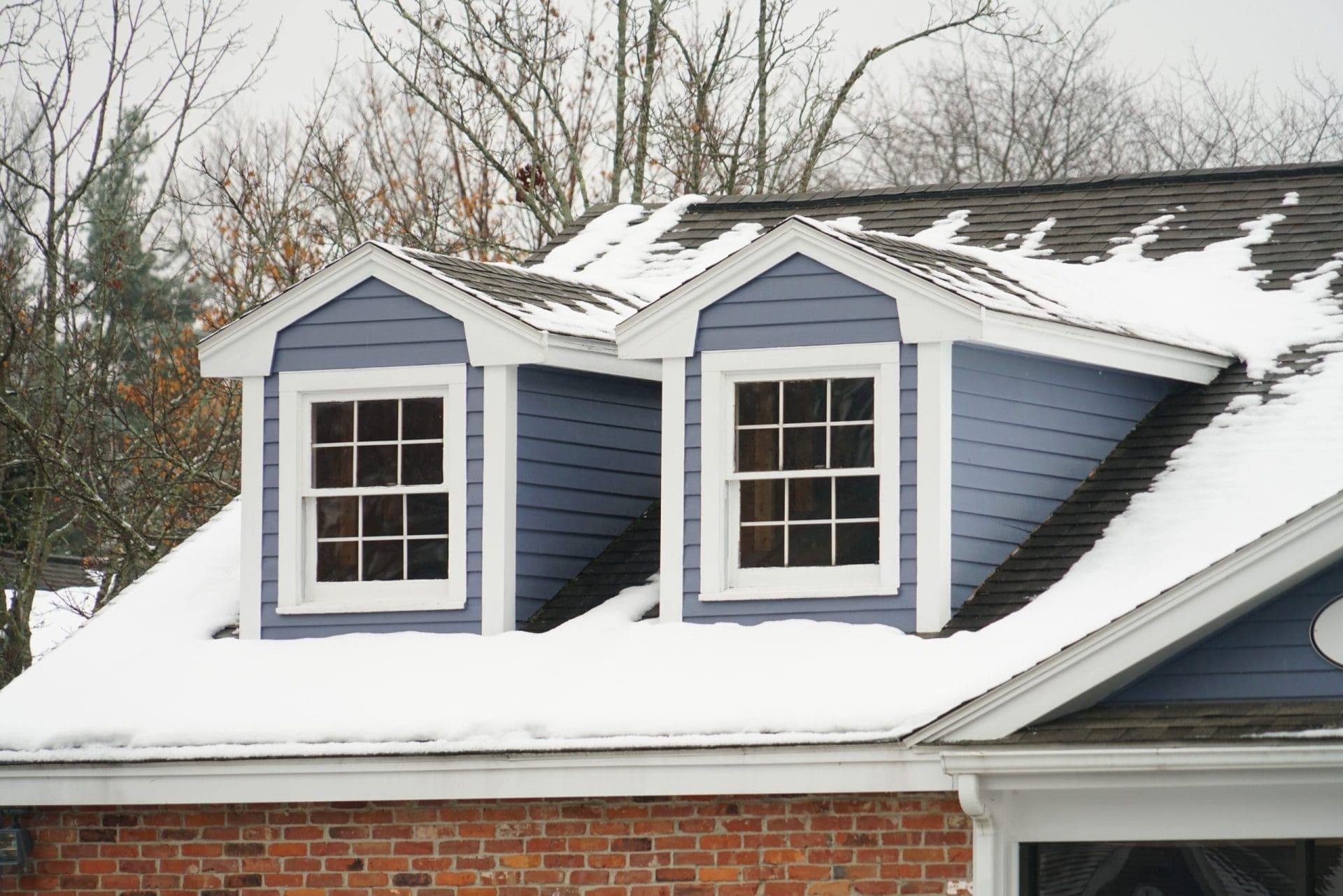 A blue roof being cleared of snow with a blue roof rake. Snow is falling off the edge, and icicles are hanging from the eaves.
