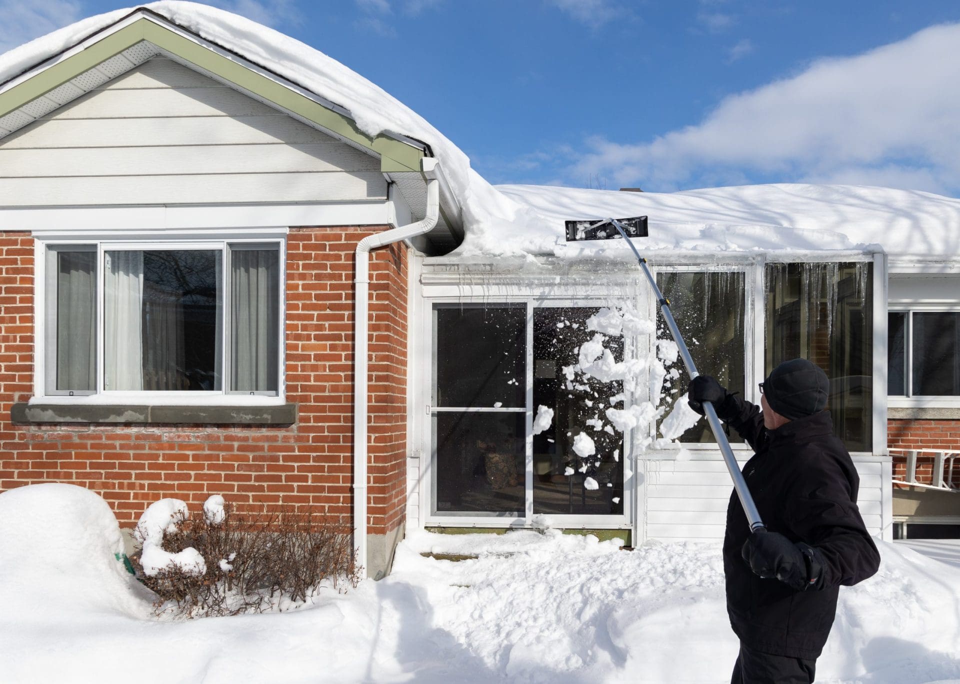Man shoveling snow out of house roof.