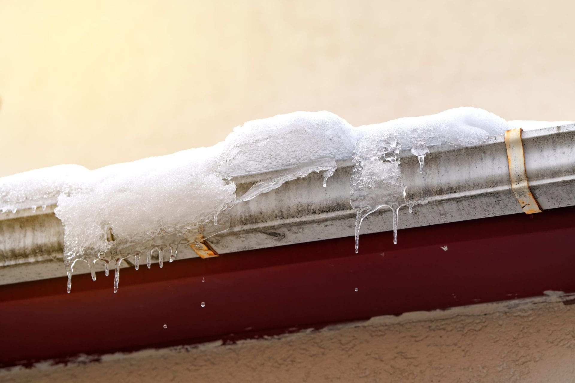 A snow-covered gutter with icicles hanging down, indicating winter buildup and potential ice damming.
