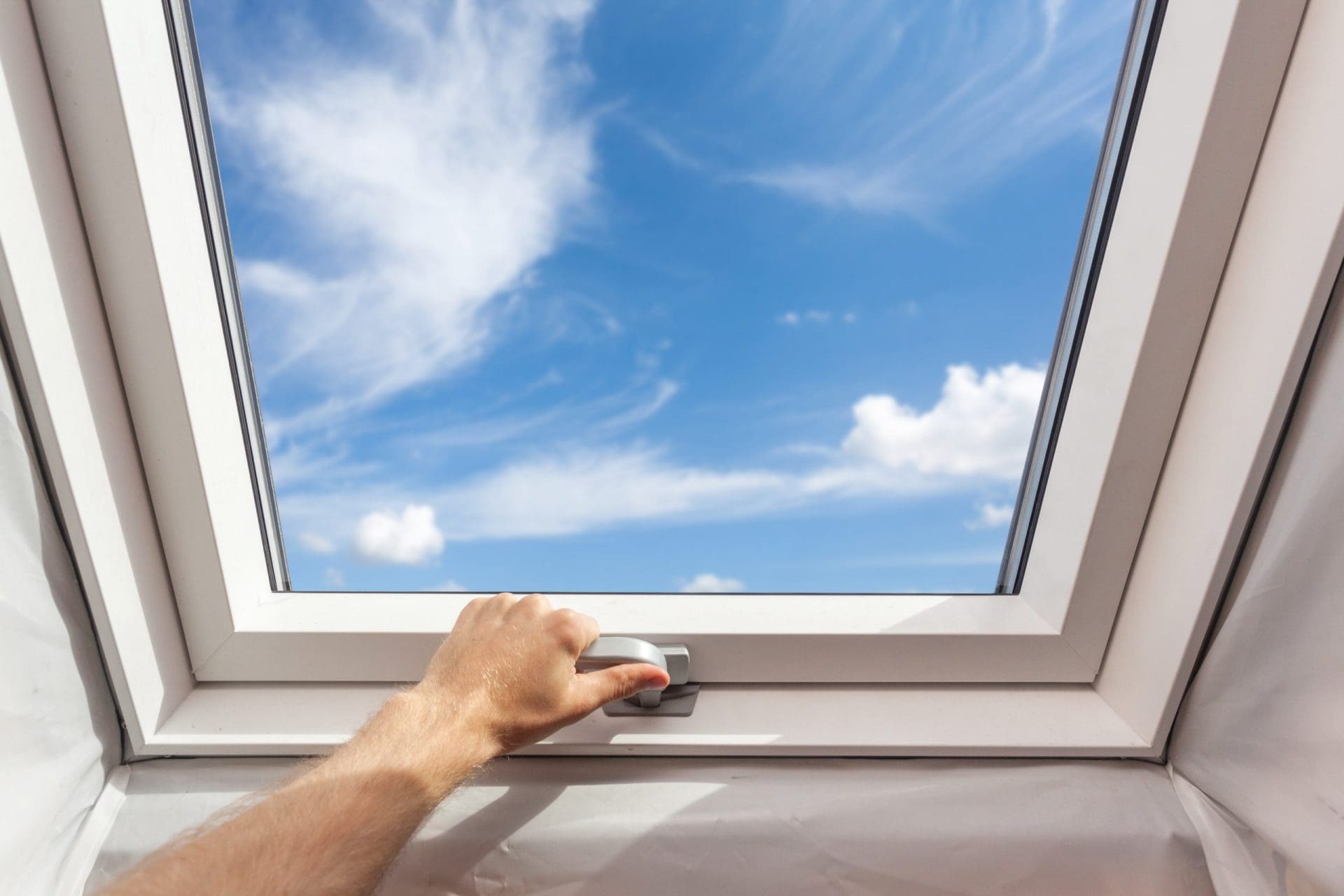 Man close new skylight (mansard window) in an attic room against blue sky.