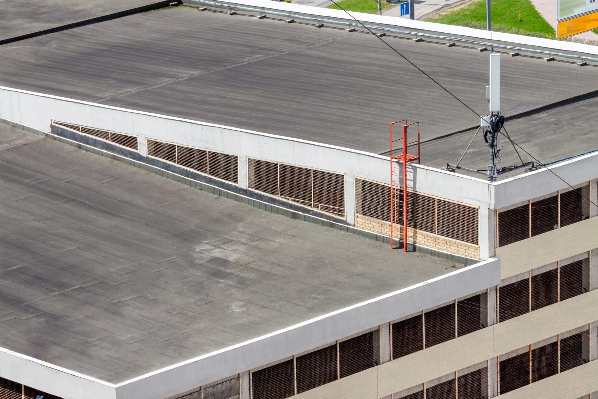 Flat roof top with antenna system and ladder on modern commercial building.