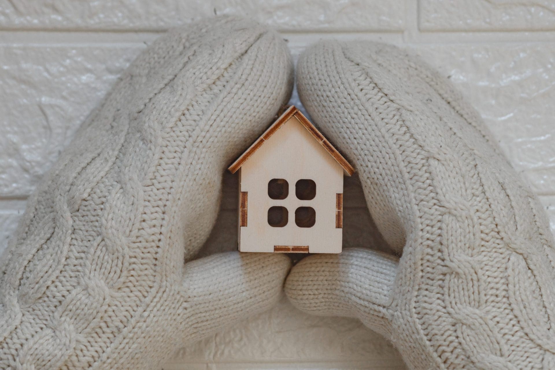 House insulation concept with hands wearing woolen mittens holding a wooden model of house.