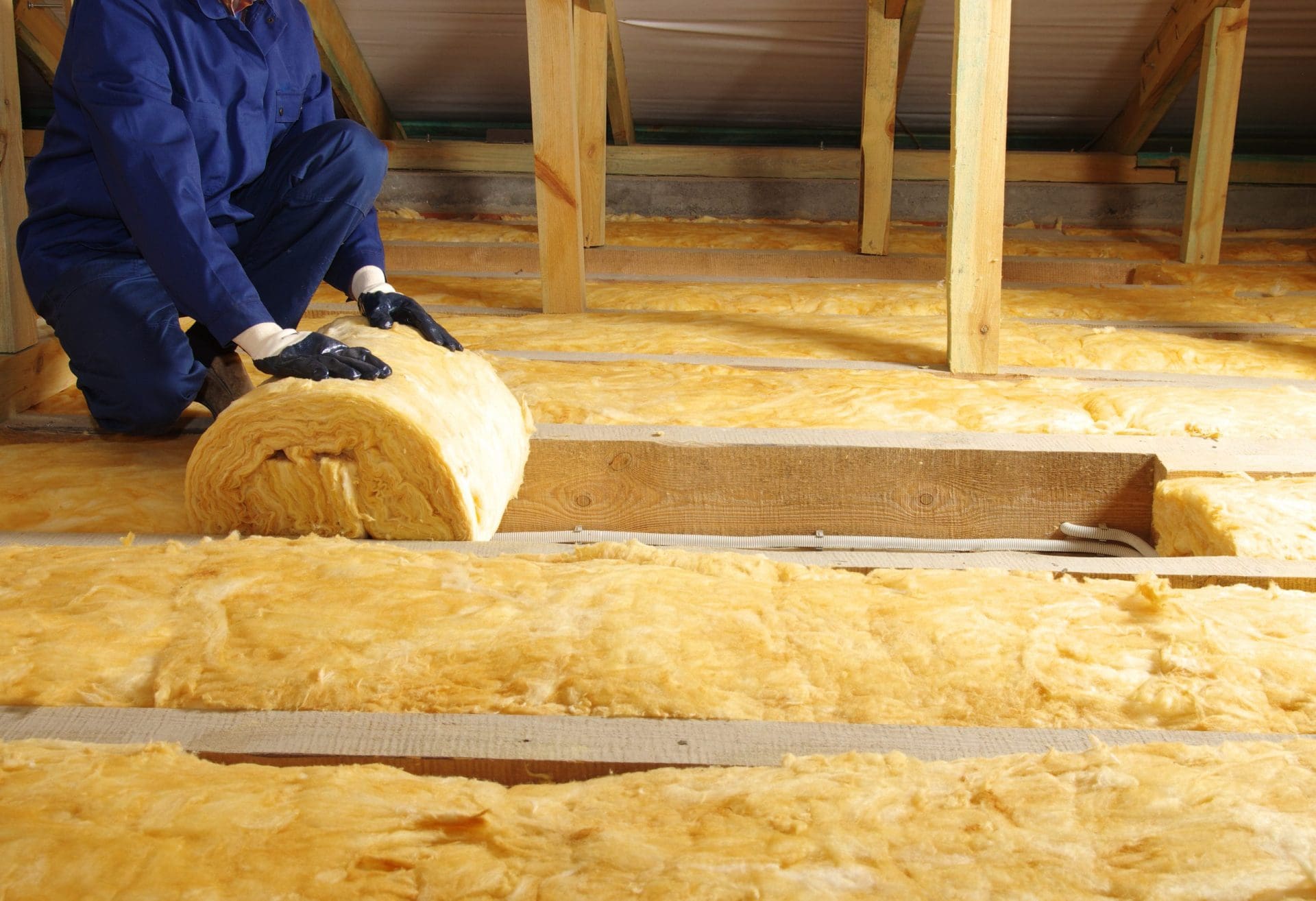 Construction worker thermally insulating house attic with glass wool.