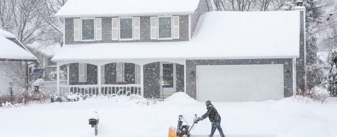 Man using a snowblower to clear his sidewalk and driveway.