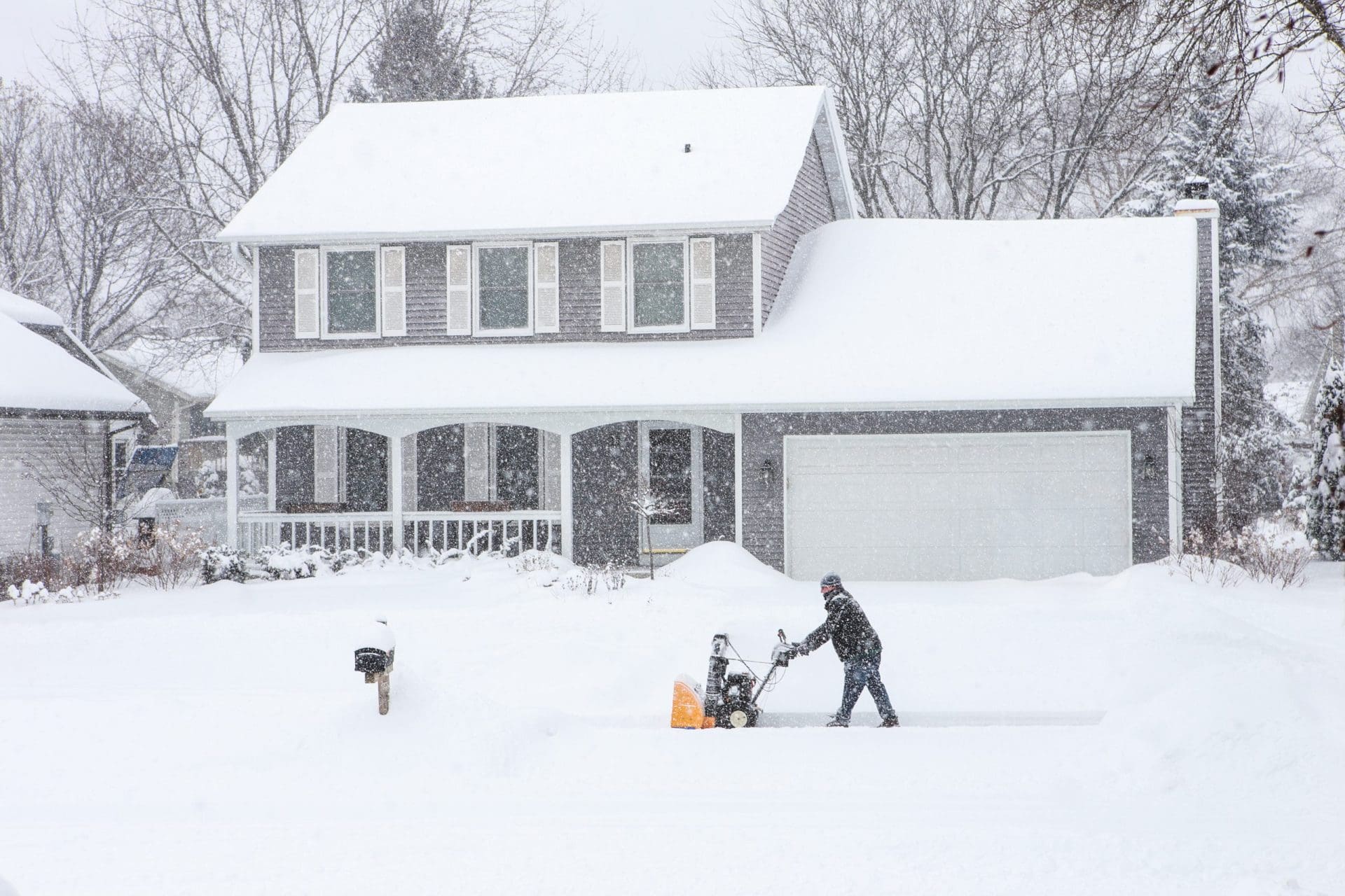 Man using a snowblower to clear his sidewalk and driveway.