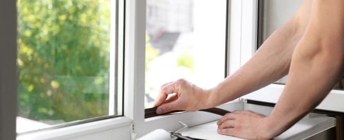 Man putting sealing foam tape on window indoors.