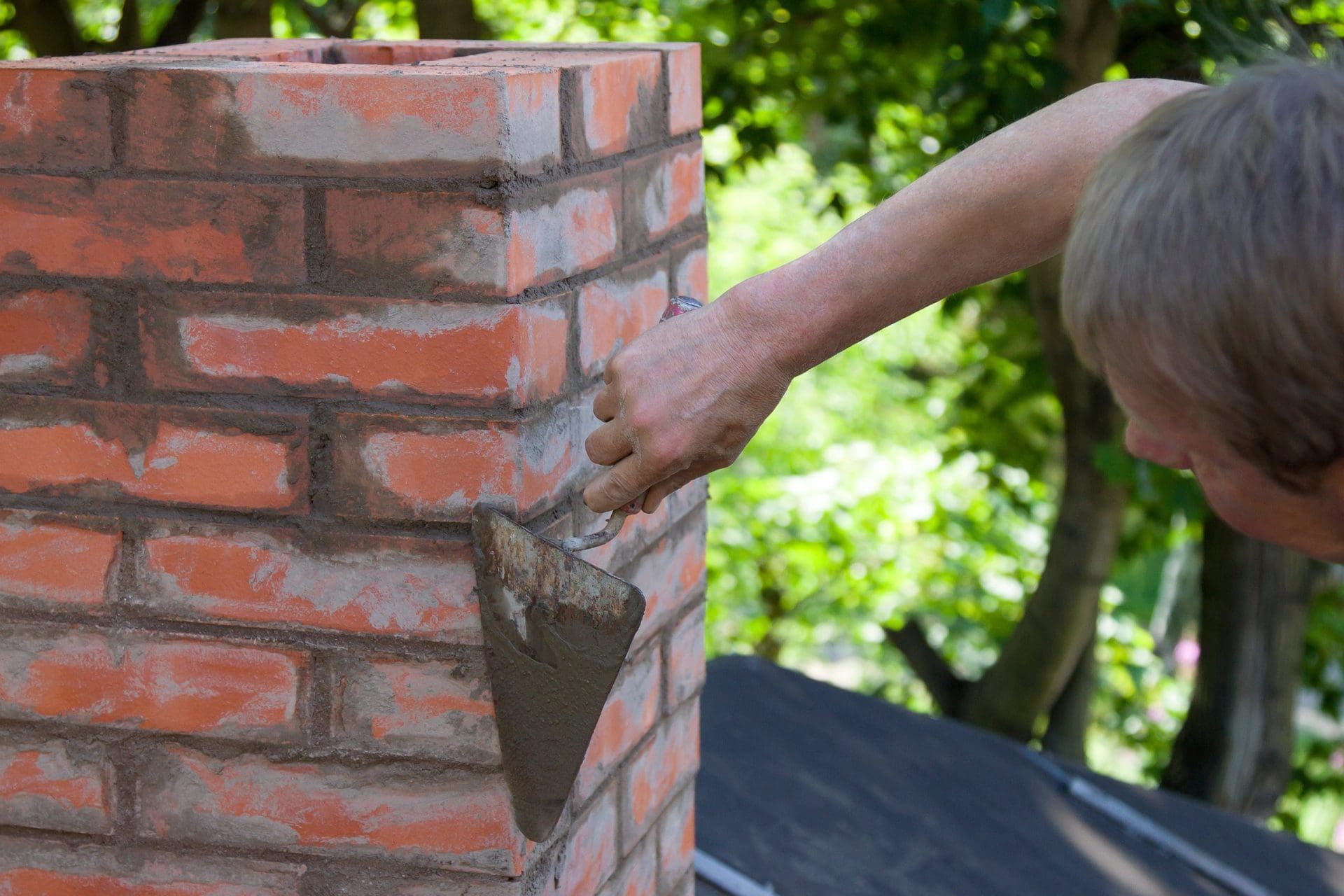Brick chimney installed on oldcement roof under with clear blue sky.