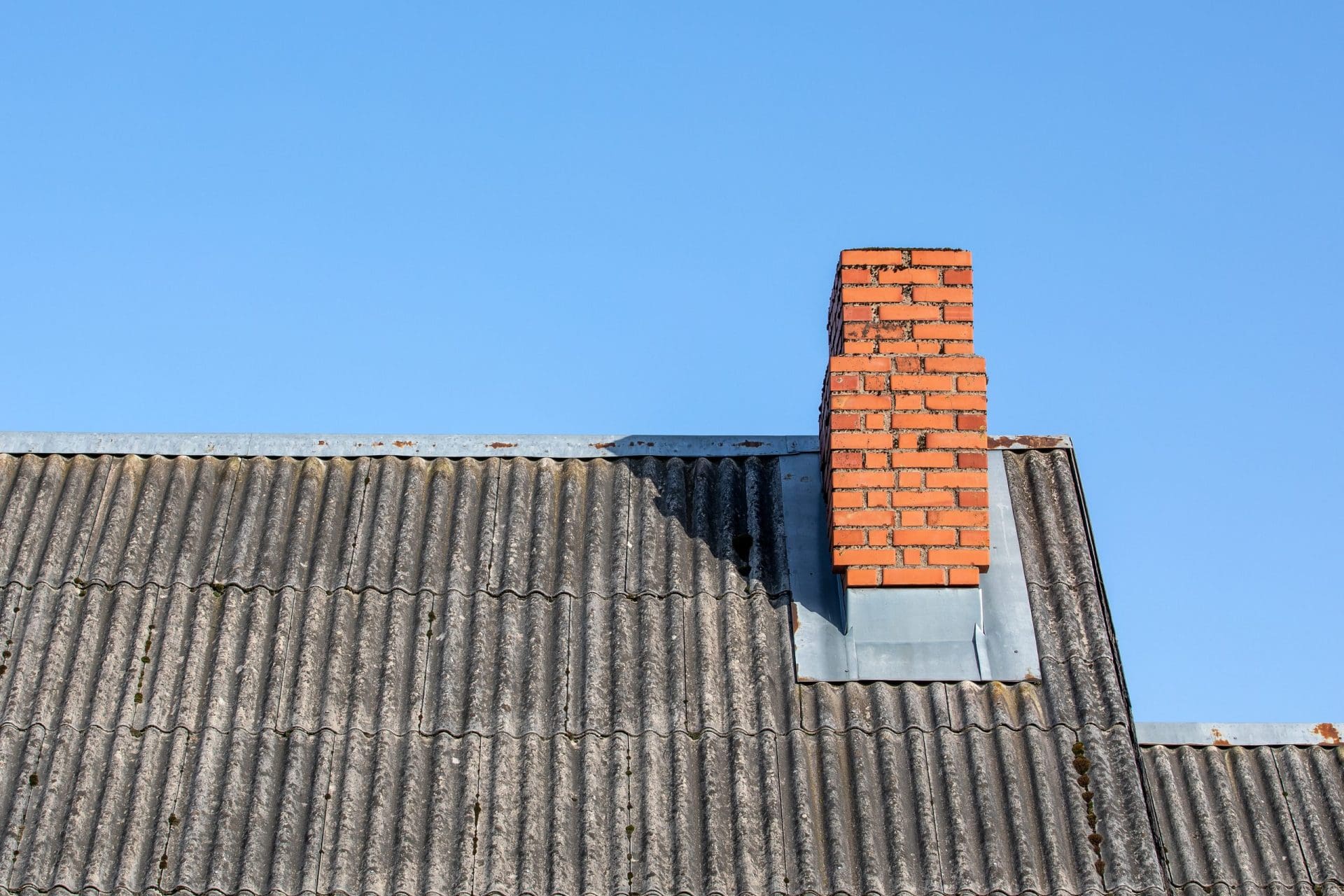 Brick chimney installed on oldcement roof under with clear blue sky.
