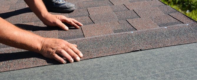 Roofing contractor lay asphalt shingles tiles on house rooftop.