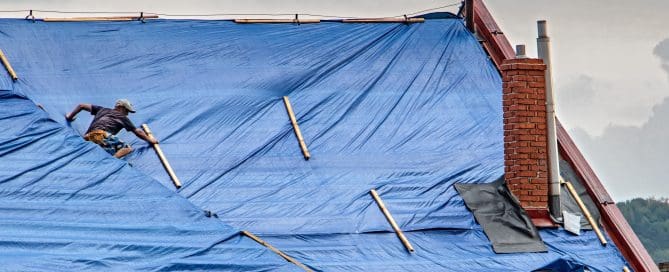 The roofer works on roof when is rain. The tarp covers the roof of the old house in the reconstruction.