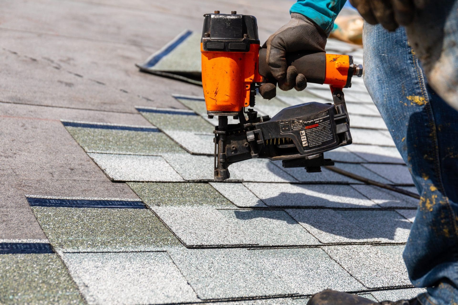 Roofer installing roof shingles with pnuematic roofing nailer.