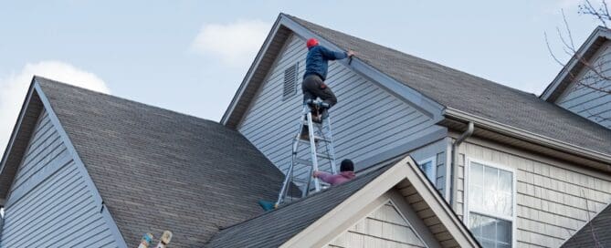 Two people work on a roof using a ladder.