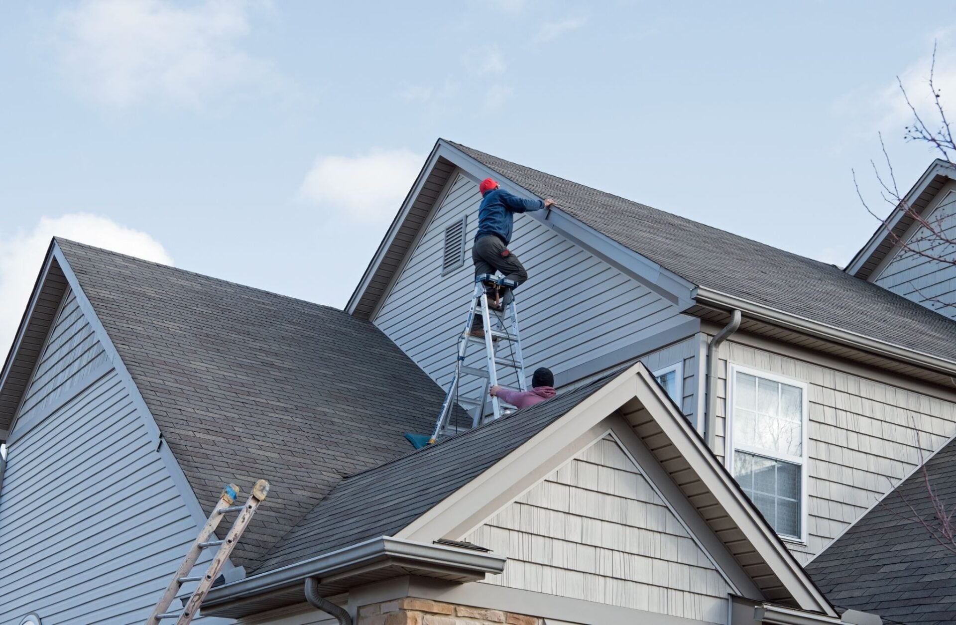 Two people work on a roof using a ladder.