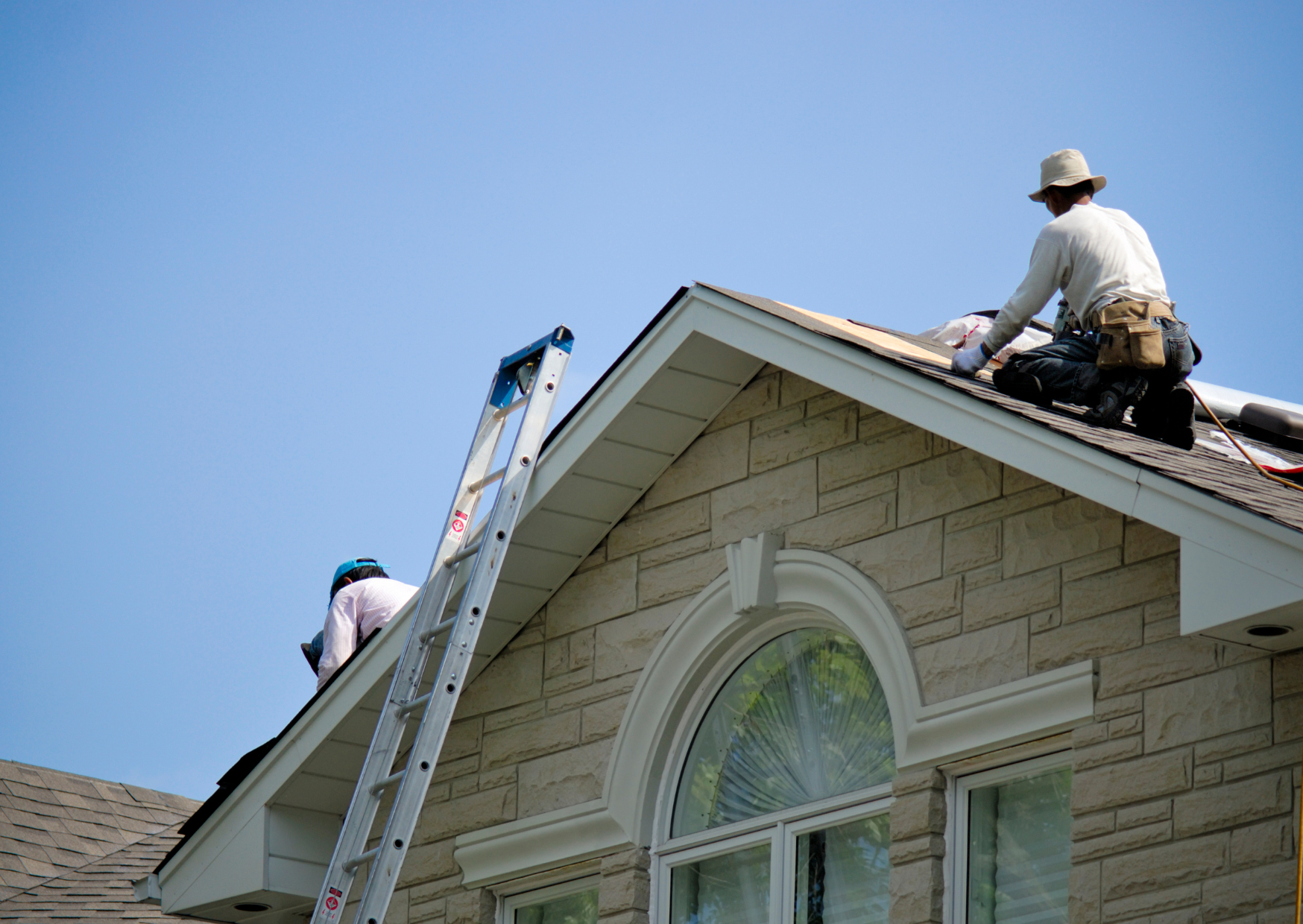 Two people working on a roof near a ladder.