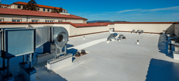 A white single ply membrane roof on a commercial building with metal rooftop ventilation units along one edge under a clear sky.