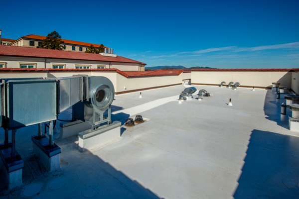 A white single ply membrane roof on a commercial building with metal rooftop ventilation units along one edge under a clear sky.